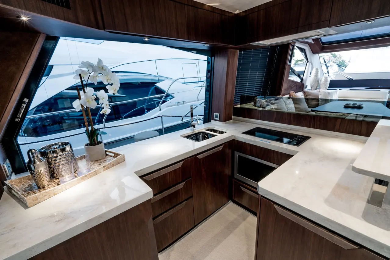 Luxurious yacht kitchen with marble countertop, flowers, sleek cabinetry, and views of yachts through large windows.