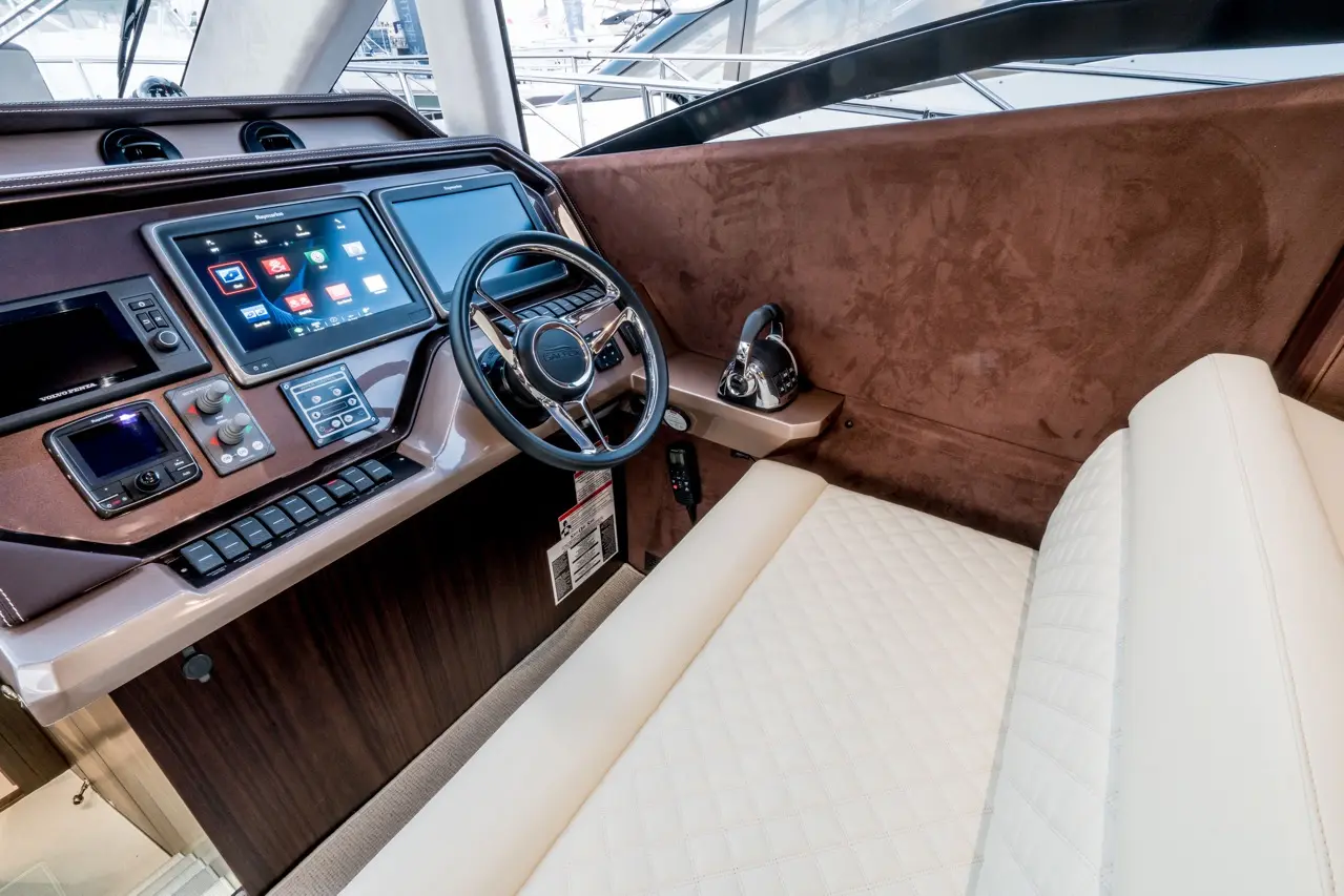 Luxury yacht cockpit featuring two digital screens, a steering wheel, control buttons, and a comfortable white seating area.