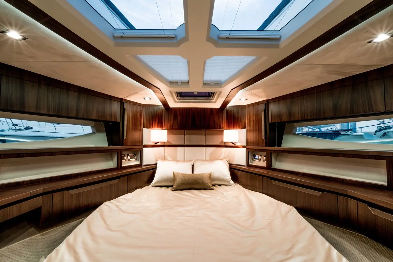 Luxurious yacht cabin featuring a large double bed, wooden furnishings, ceiling skylights, and ambient lighting.