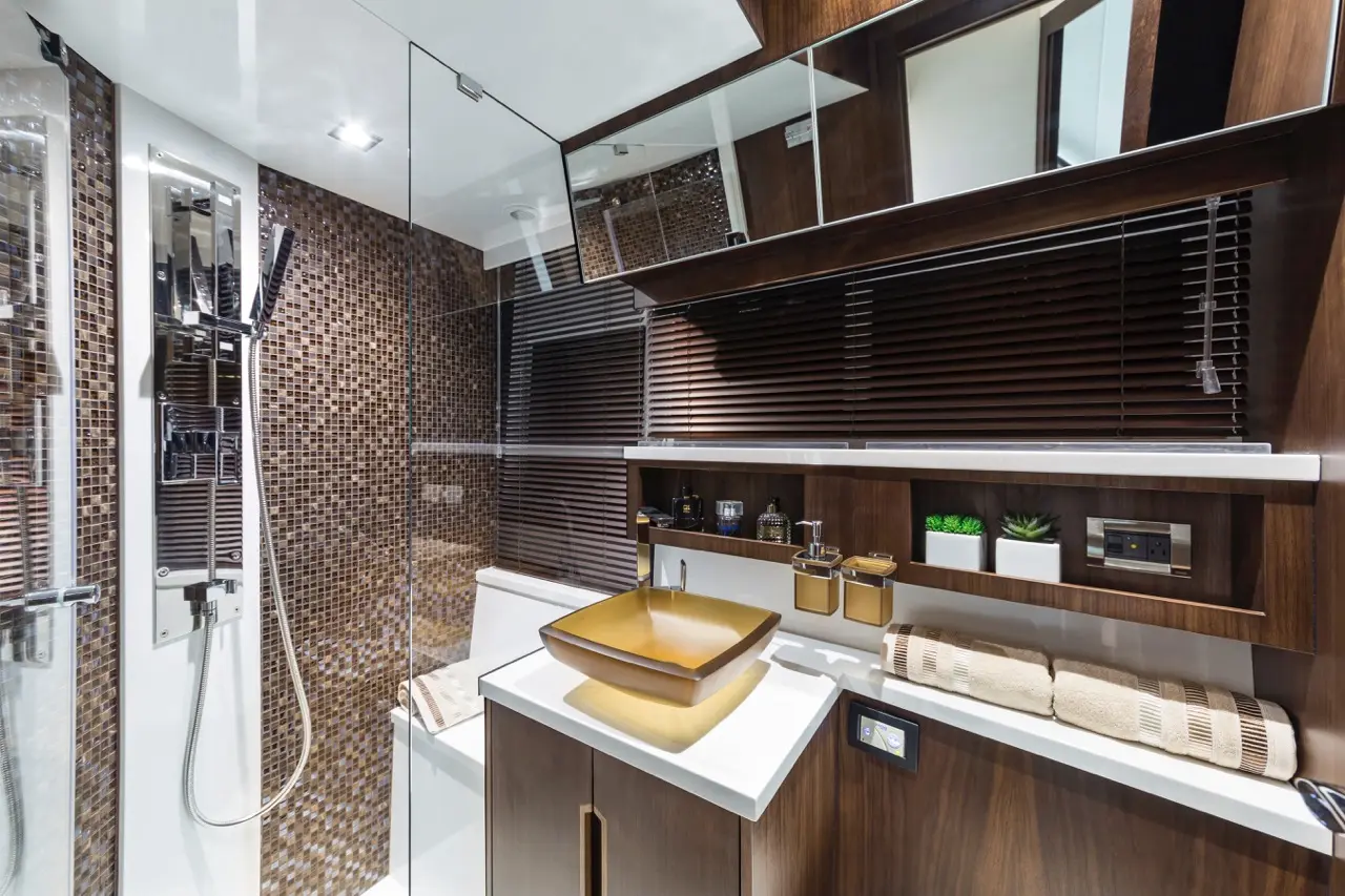 Modern bathroom featuring a glass shower, wooden accents, a square golden sink, and decorative plants on shelves.