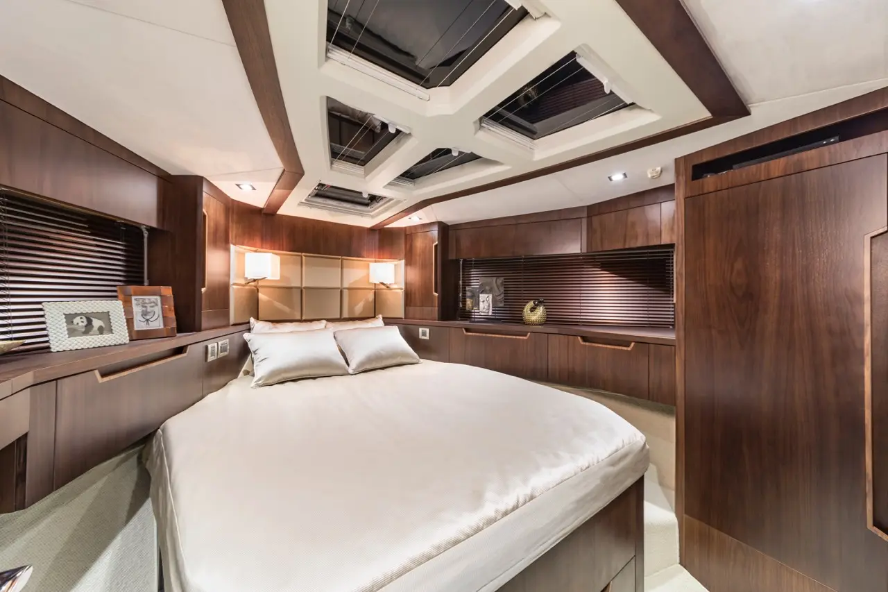 Modern boat bedroom featuring a circular bed, wooden walls, skylights, and decorative lamps. A framed photo is on the bedside table.