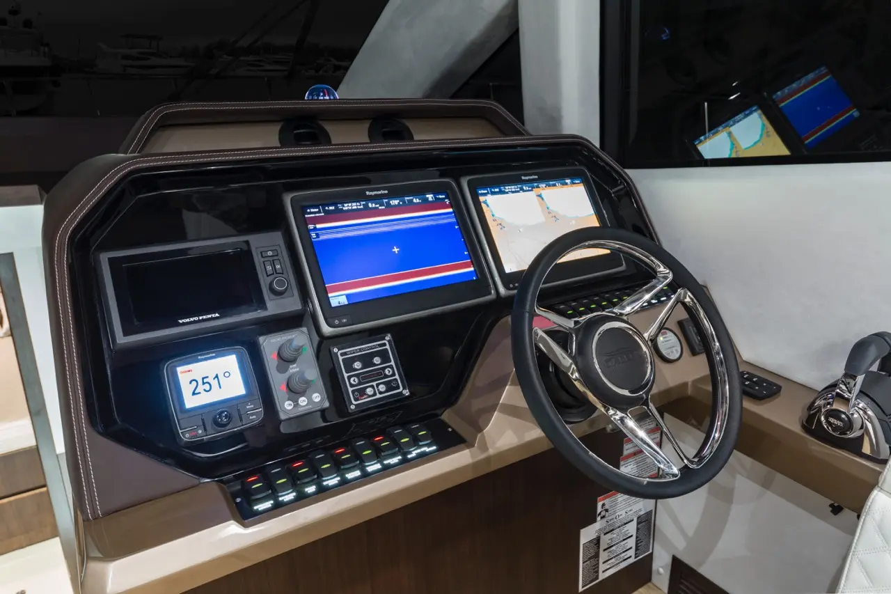 Modern boat dashboard featuring dual Raymarine displays, Volvo Penta controls, navigation screens, and a chrome steering wheel.