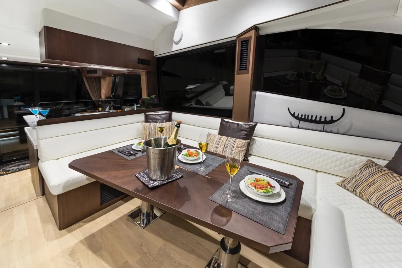 Elegant dining area on a yacht, featuring a wooden table, gourmet salads, champagne, and stylish seating with decorative pillows.
