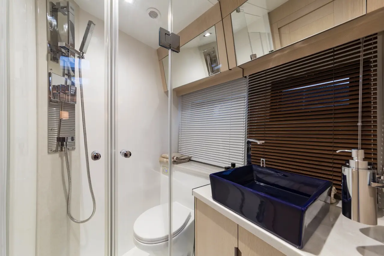 Modern bathroom with a glass shower, toilet, and a blue rectangular sink beside a window with blinds.
