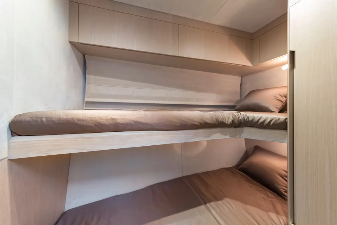 Interior of a compact sleeping space with two bunk beds and beige bedding, highlighting minimalist design and wooden cabinetry.