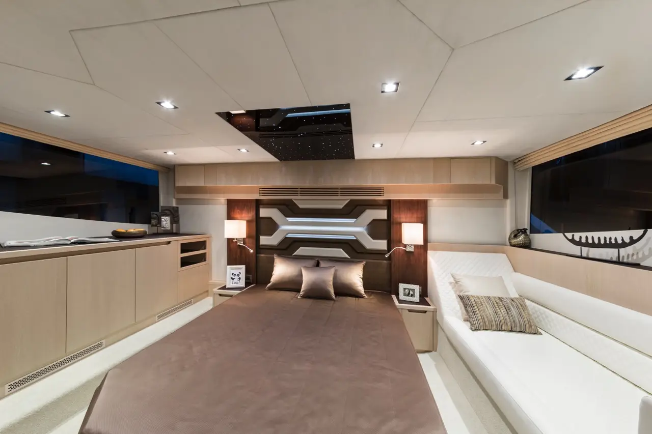 Modern yacht interior featuring a brown bedspread, accent pillows, a white sofa, and ambient lighting. Sleek design elements throughout.