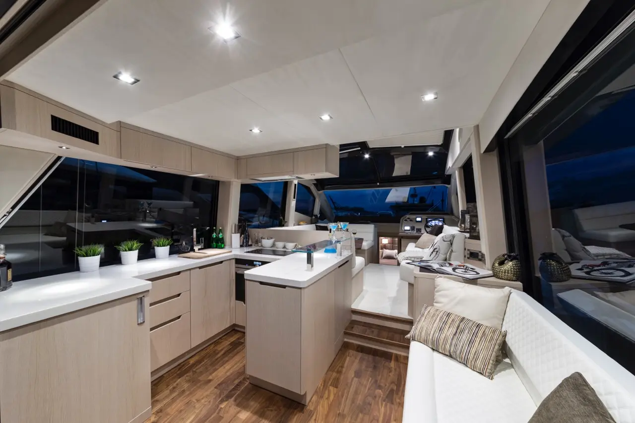Modern yacht interior featuring a sleek kitchen with a white countertop, wooden accents, and large windows showcasing the night view.