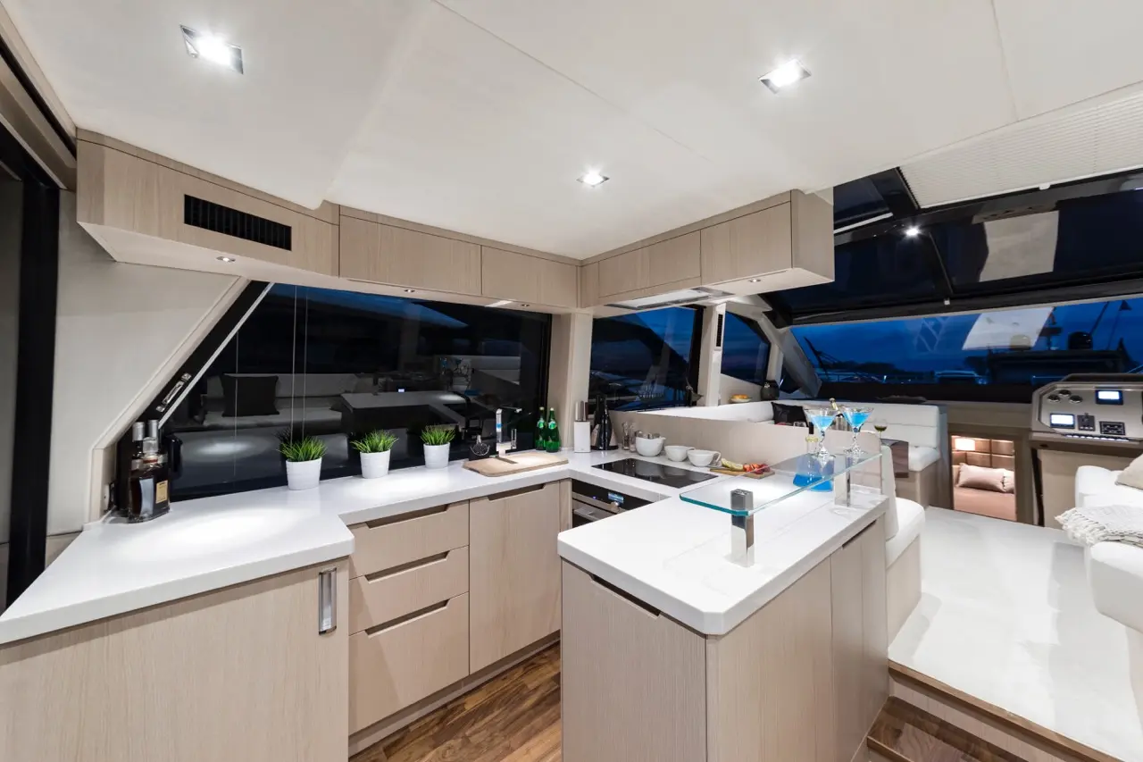 Modern yacht kitchen featuring sleek cabinetry, large windows, and dining area with glasses, dishes, and decorative plants.