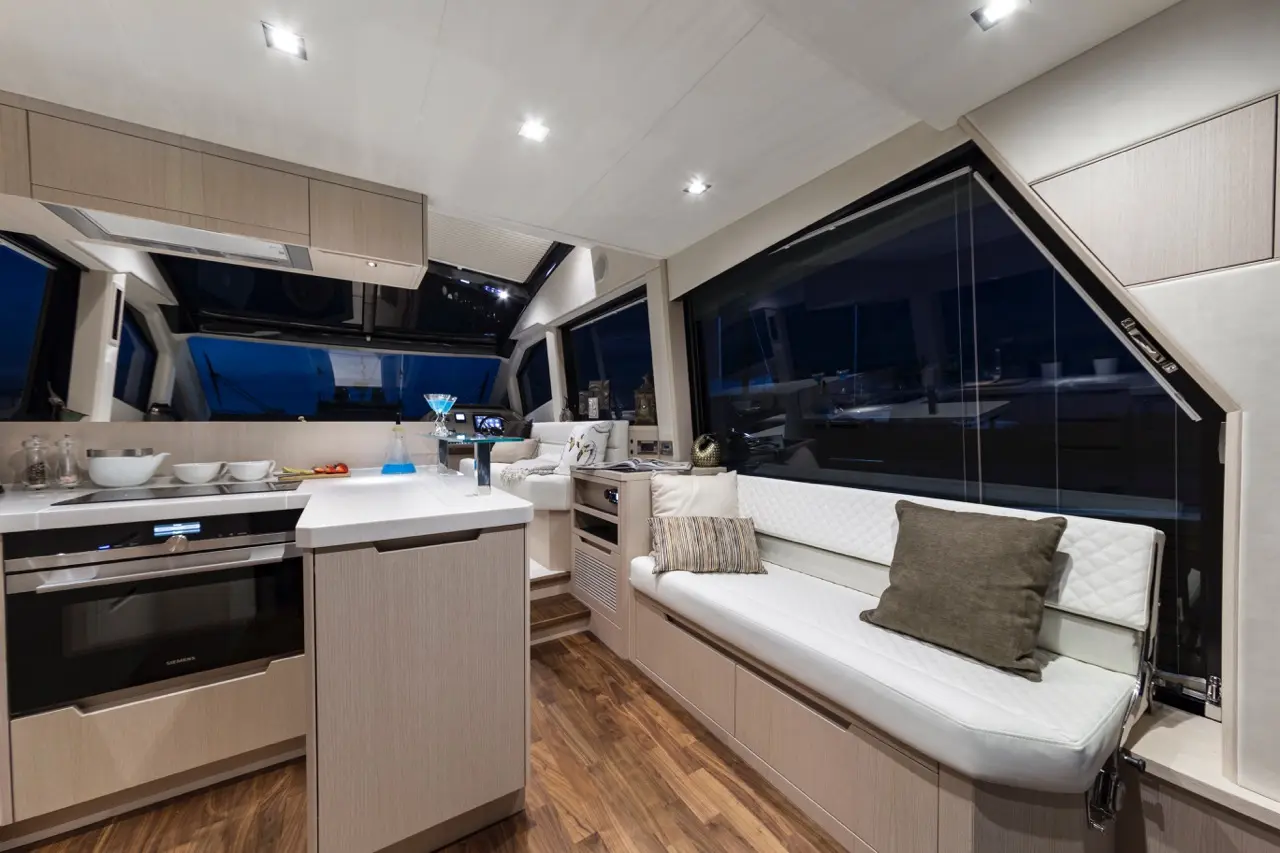 Modern yacht interior with kitchenette, seating area, large windows, and ambient lighting, creating a luxurious atmosphere.