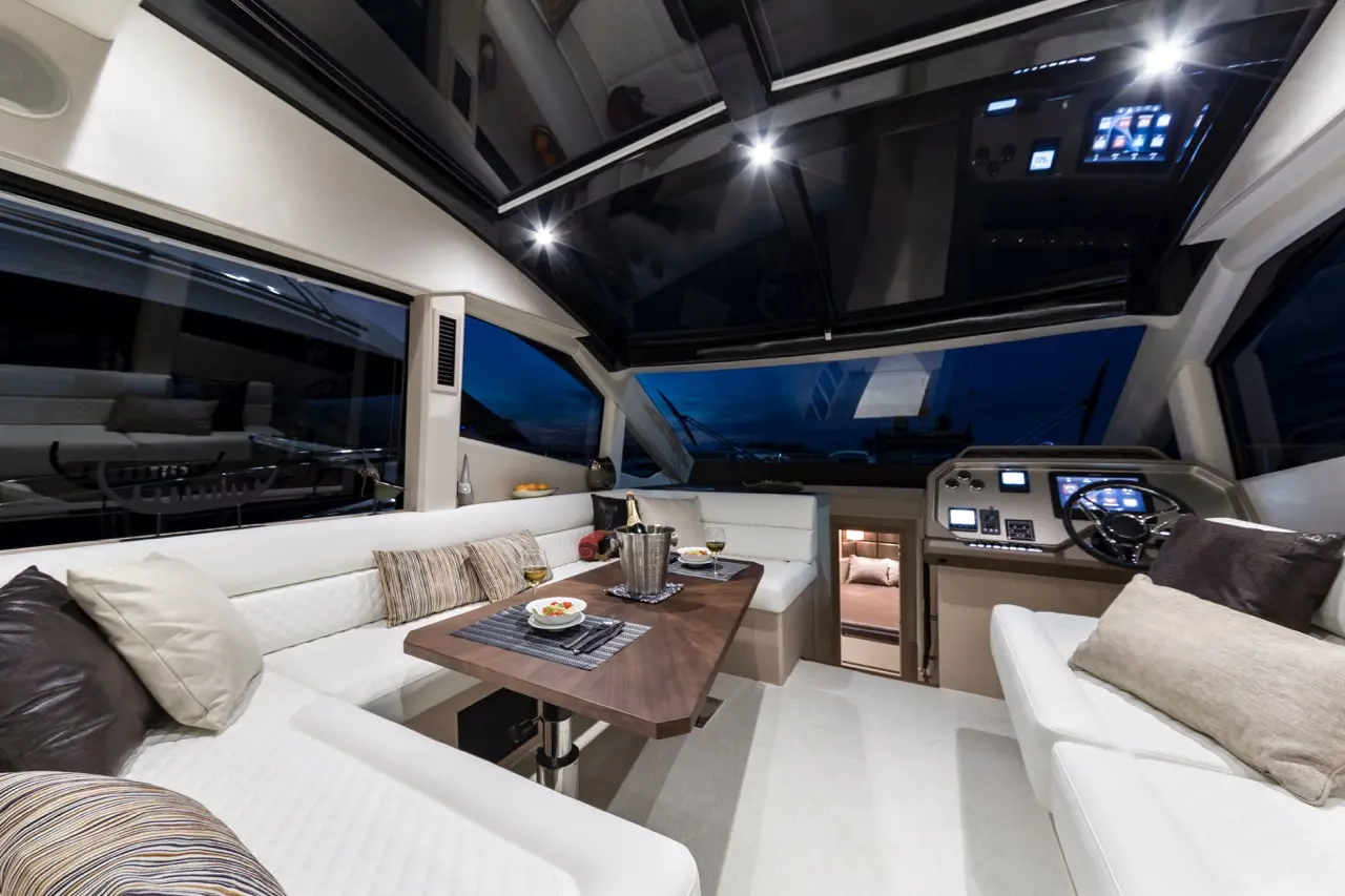 Luxury yacht interior featuring a dining area with a table, plush seating, and a control panel, illuminated at night.