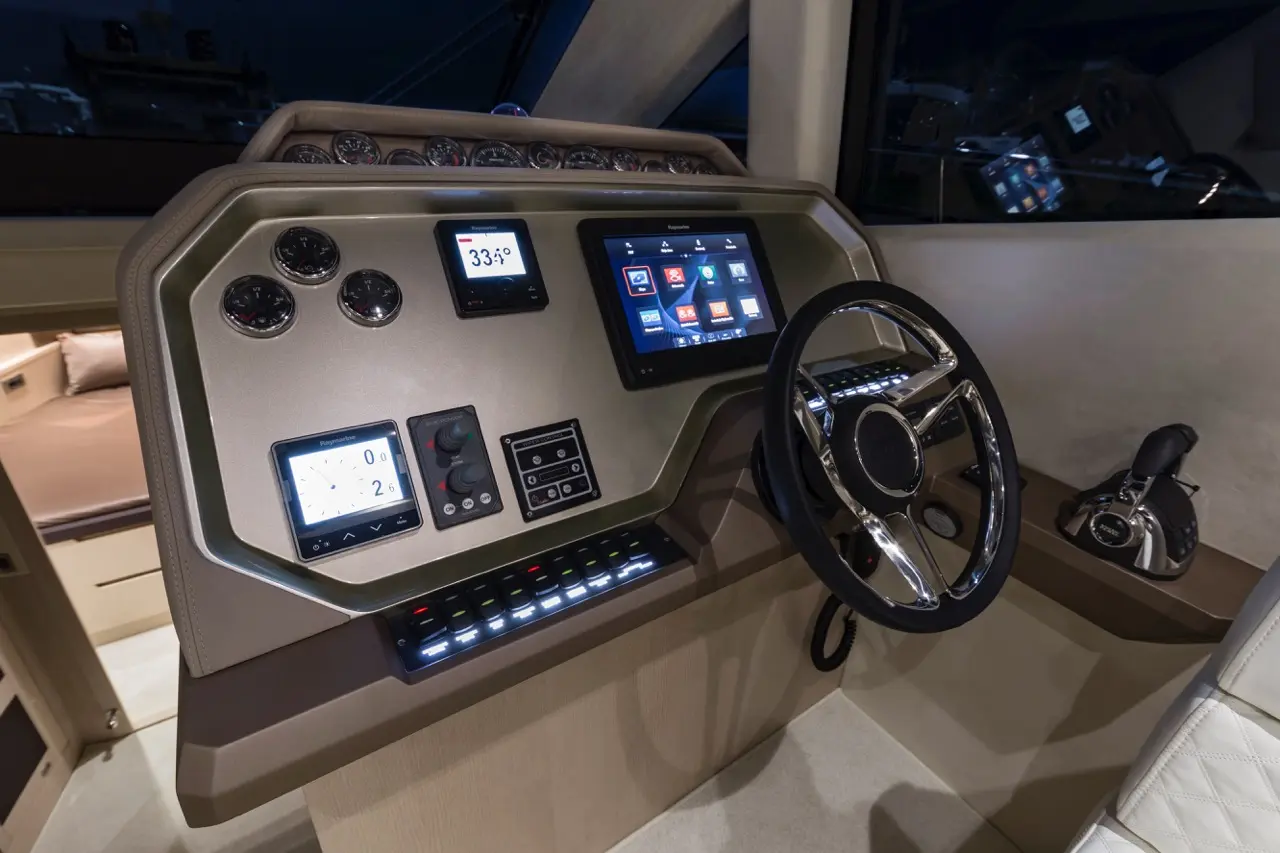 Modern boat dashboard features digital screens, various gauges, controls, and a sleek steering wheel in a contemporary design.