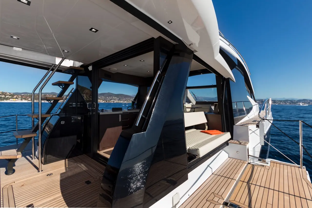 Luxurious yacht interior with sleek black glass, steering area, and wooden steps leading to the deck and scenic ocean view.