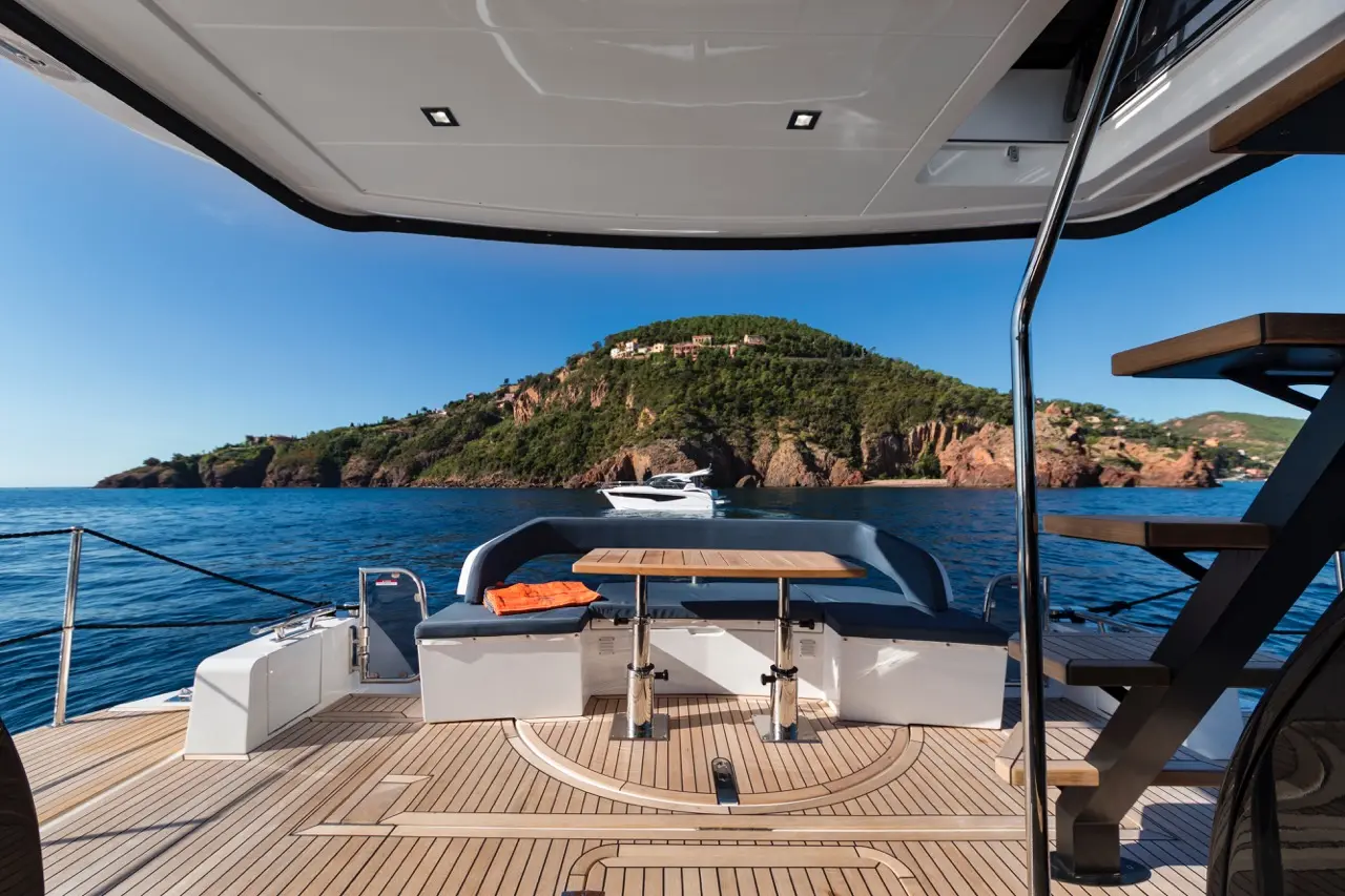 Luxury yacht deck with a table, seating, and a scenic mountain view across calm waters, under clear blue skies.