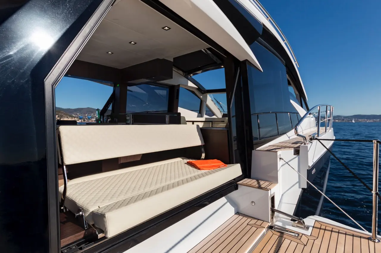 Luxury yacht interior showing a lounge area with a beige bench and an orange towel, overlooking a scenic marina view.