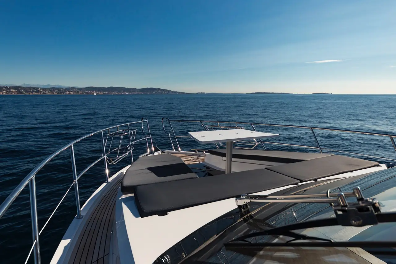 Luxury yacht deck overlooking the tranquil sea, featuring lounging pads and a small table, with a scenic coastline in the background.