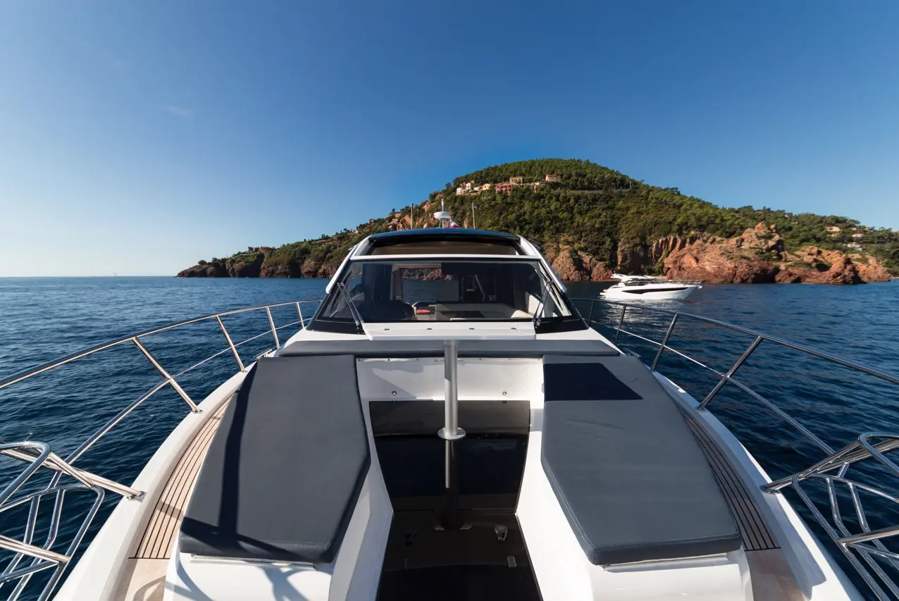 Luxury yacht bow facing a serene coastline with rocky cliffs and green hills under a clear blue sky and calm waters.