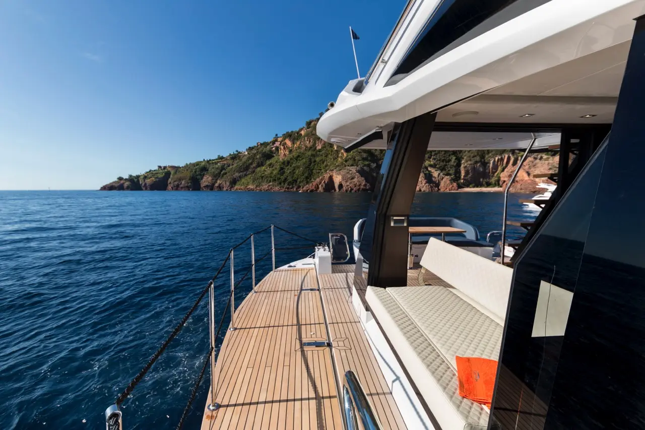 Luxury yacht view with a sunlit deck, coastline in the background, and an orange notebook on a white sofa.