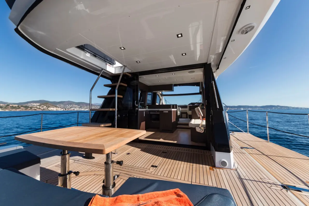 Luxury yacht interior featuring a wooden table, stairs to a cabin, and scenic ocean views under a clear blue sky.