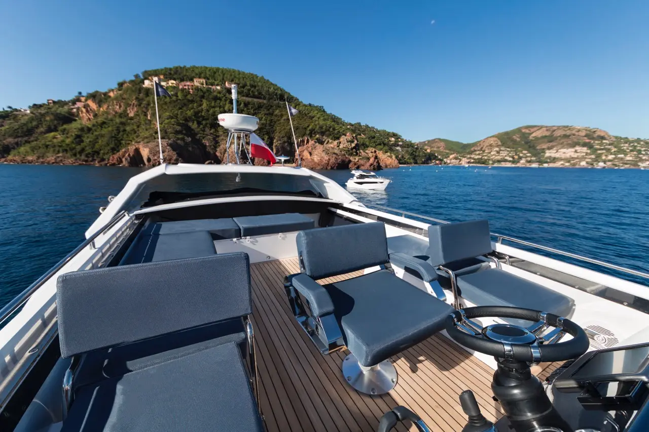 Luxury yacht deck with grey seating, steering wheel, and scenic coastline in the background under a clear blue sky.