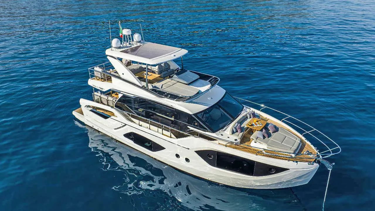 Luxury white motor yacht cruising on deep blue sea, viewed from above, with spacious sun decks, flybridge and outdoor seating