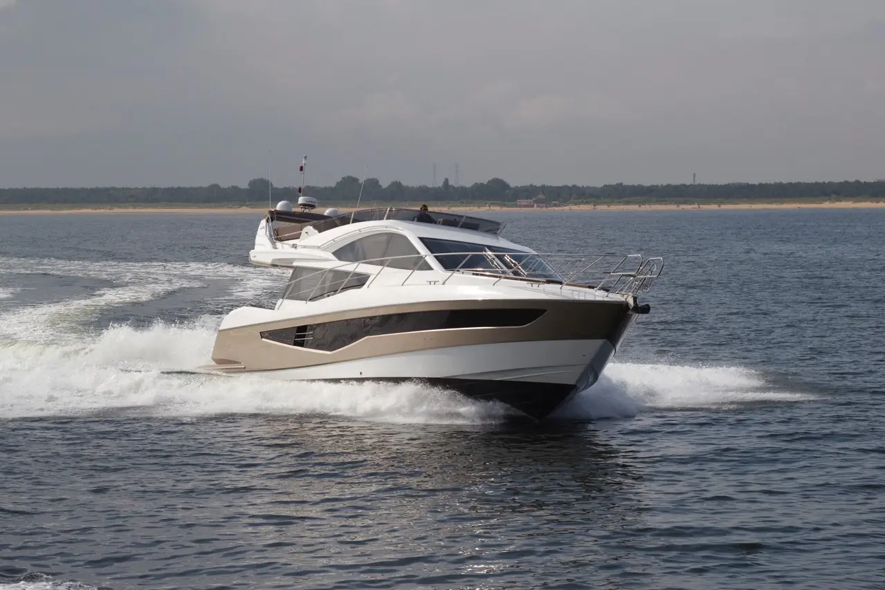 A sleek motor yacht speeds through calm waters, leaving a white wake behind, under a partly cloudy sky.
