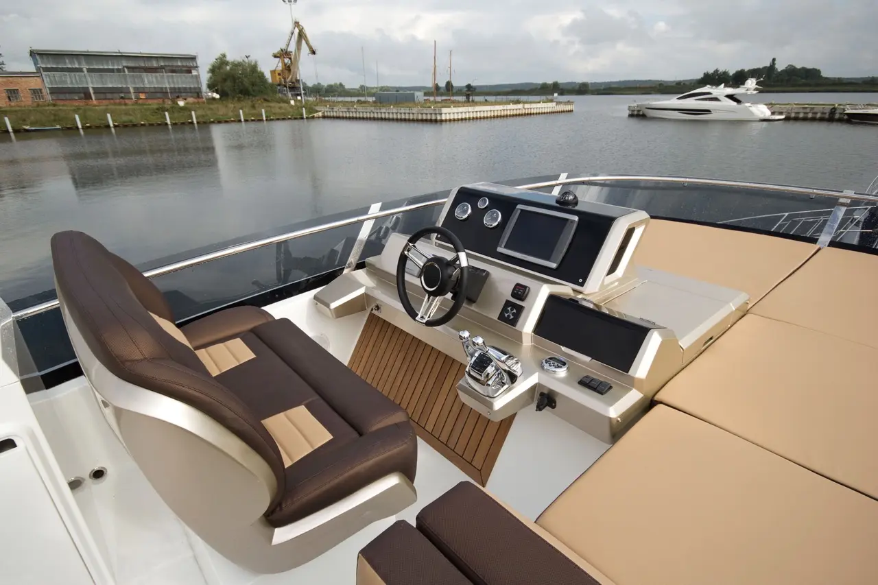 Luxury boat cockpit with modern steering wheel, digital screens, and comfortable seating, overlooking calm water and dock.