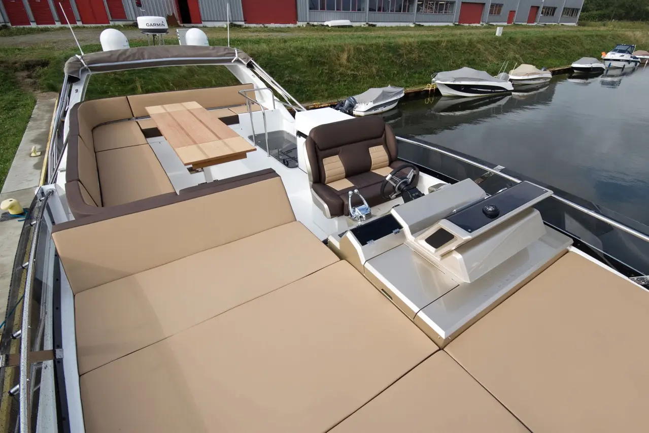 A spacious boat deck with tan cushions, a wooden table, and a leather captain's chair near navigation controls.