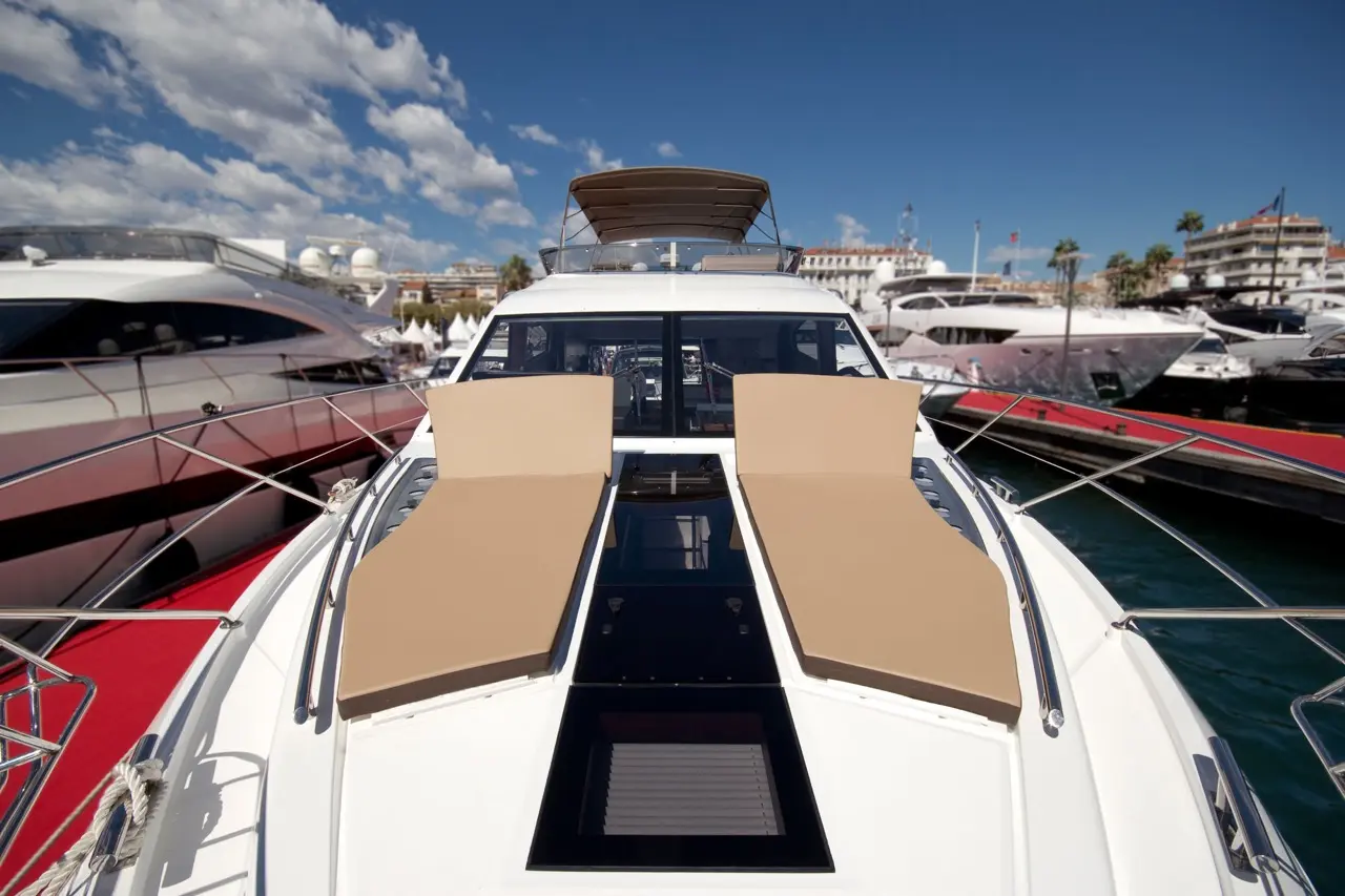 Luxury yacht with cream sun loungers on deck, moored in a marina under a blue sky with scattered clouds.