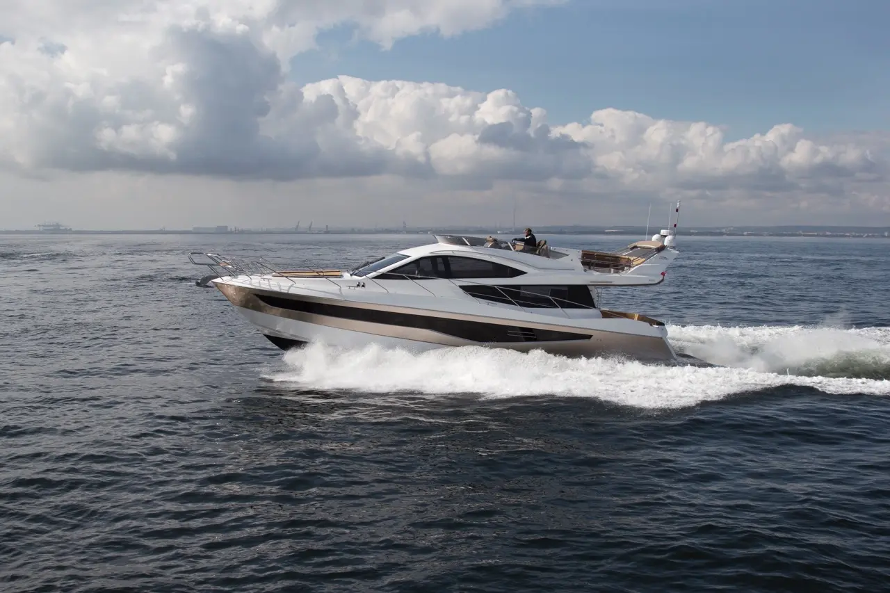 Luxury yacht cruising on wavy water, emitting spray, under a partly cloudy sky. Perfect for leisure boating activities.
