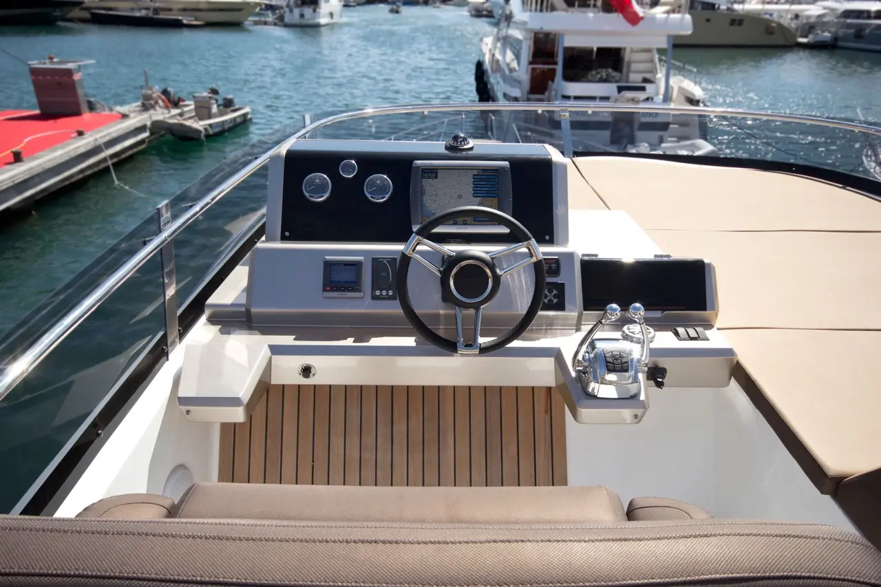 Boat cockpit with steering wheel, digital display, navigational instruments, and marine features overlooking the water.