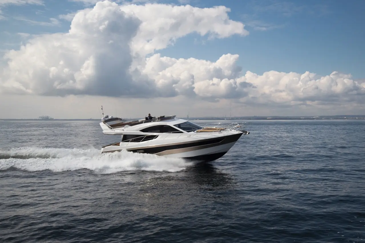 A sleek luxury yacht navigating through calm waters under a cloudy sky, leaving a wake behind.