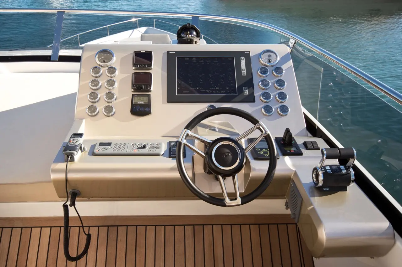 Luxury yacht control panel featuring a steering wheel, navigation displays, gauges, and communication equipment on a sunny day.