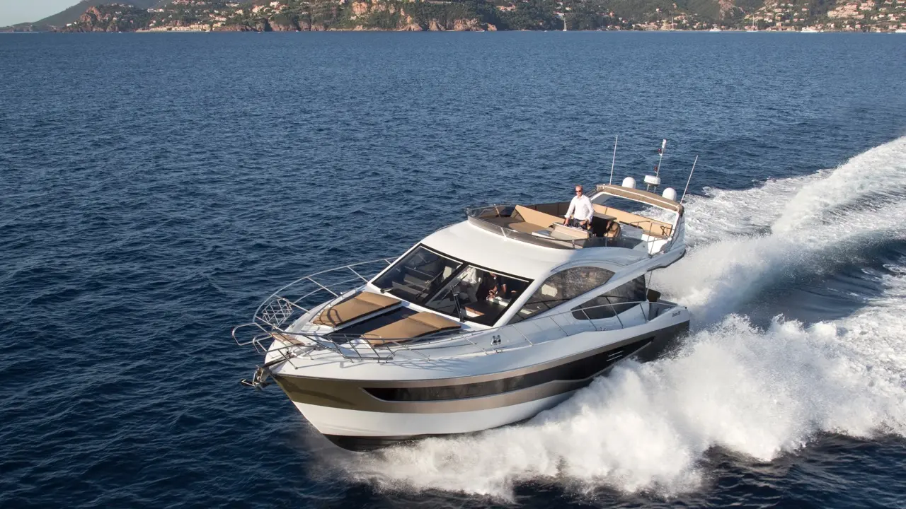 Luxury yacht cruising through blue waters, with a captain at the helm and scenic coastline in the background.