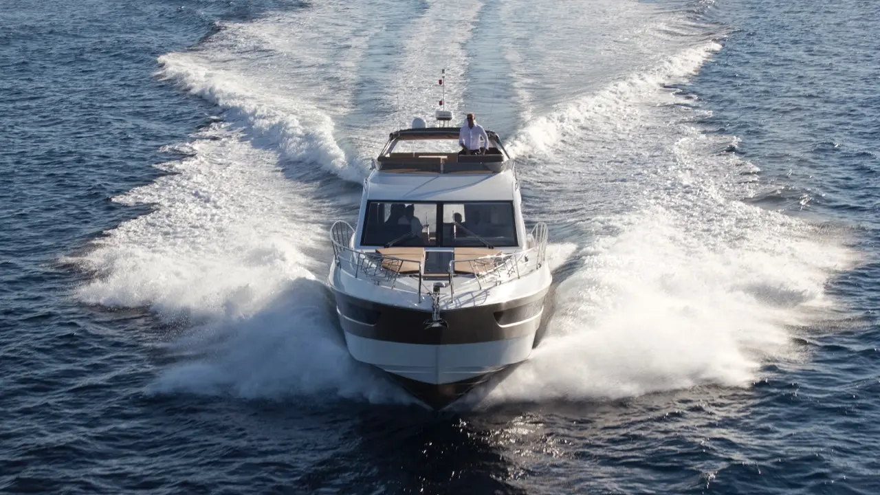 A luxury motorboat cruises through blue waters, leaving a wake; a man steers from the bridge, enjoying the sunny day.