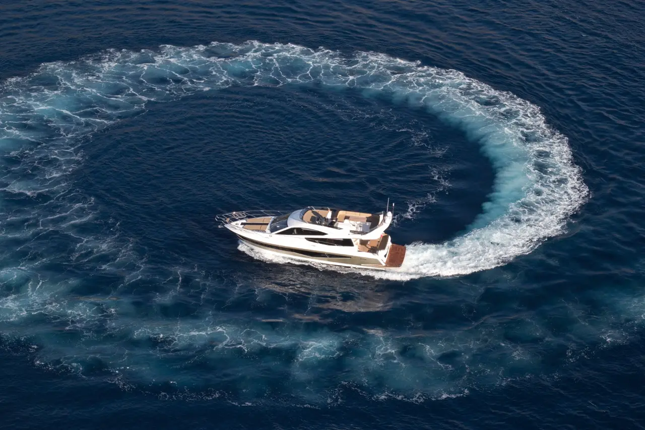 A luxury yacht sailing in a circular path, creating ripples and wake in the deep blue ocean water.