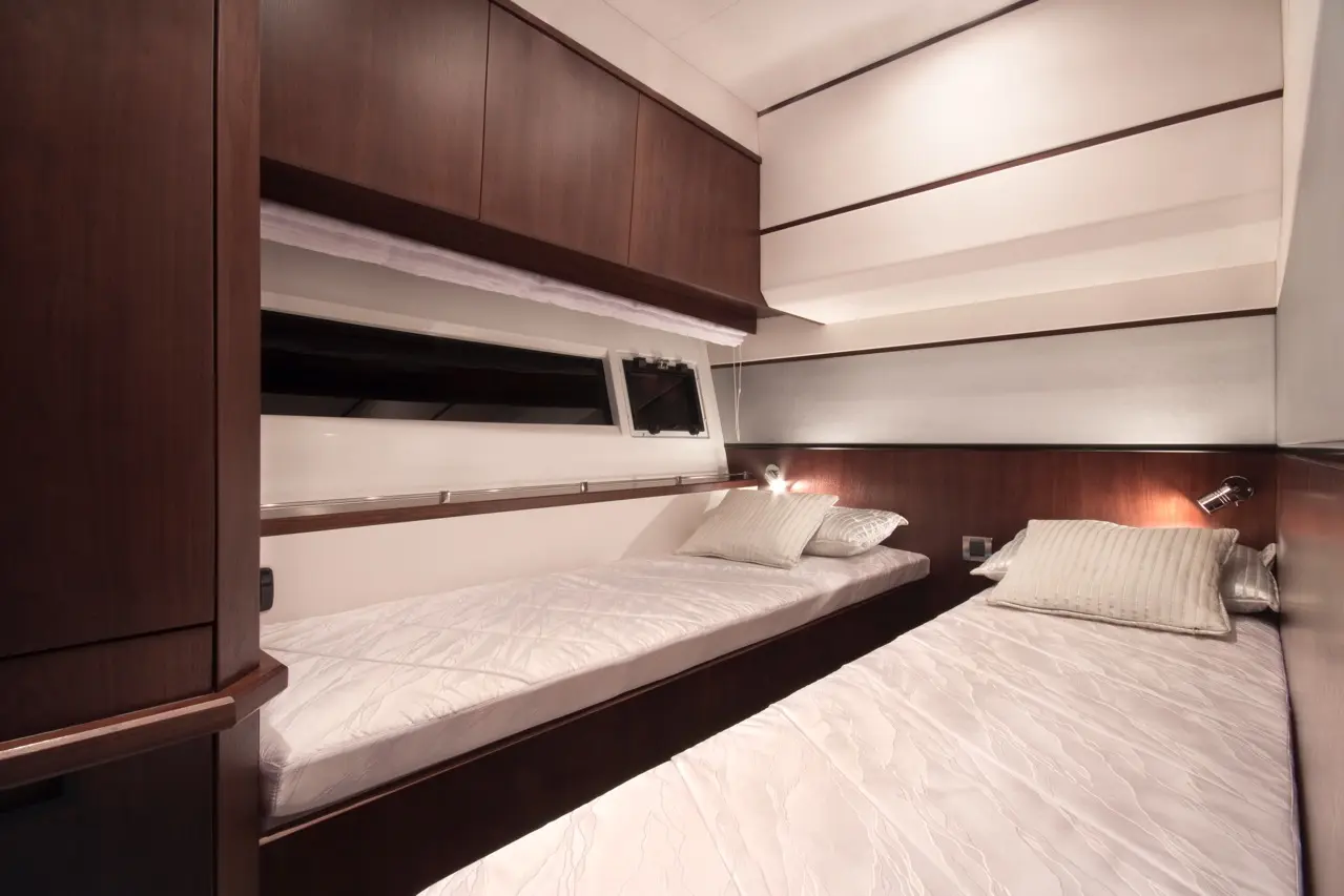 Cozy yacht cabin featuring two twin beds with white linens, wooden cabinetry, and wall-mounted reading lights.