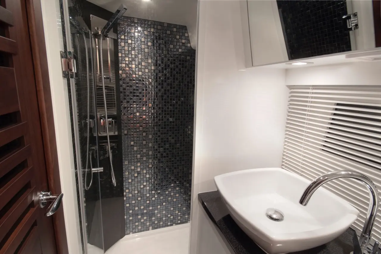 Modern bathroom with a sleek shower featuring black mosaic tiles, a white sink, and neutral decor.