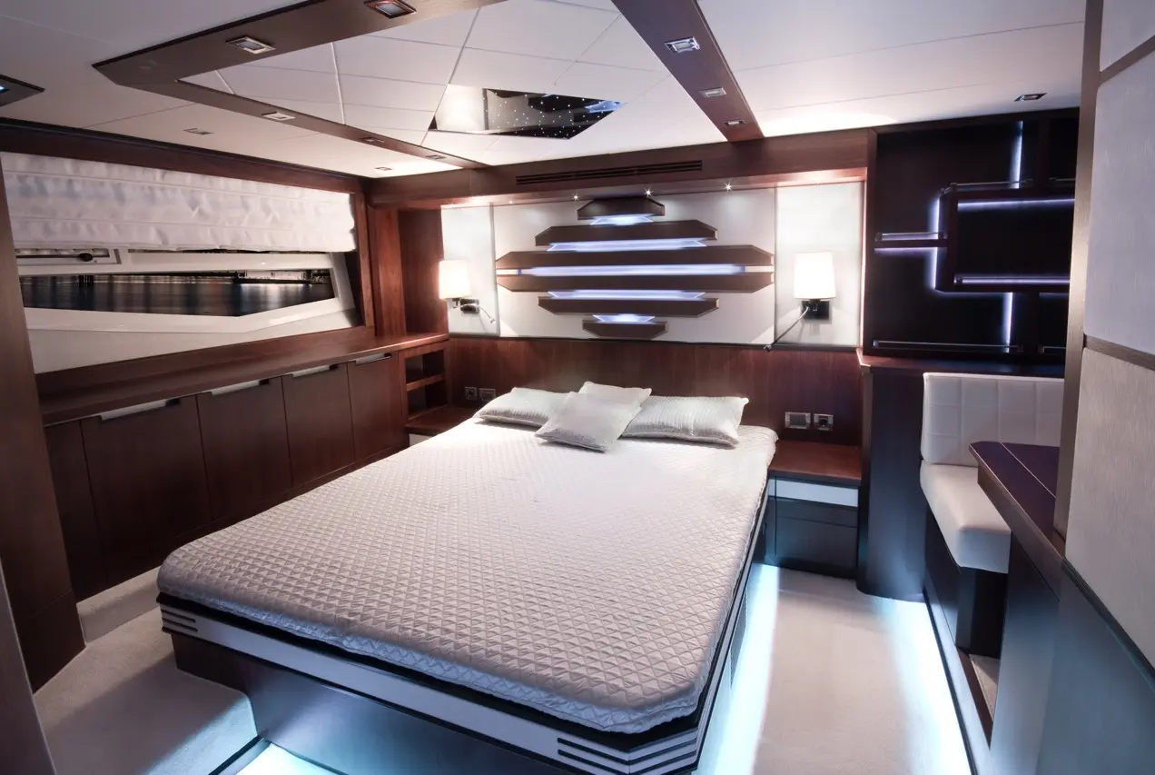 Modern yacht interior featuring a double bed, stylish lighting, wooden cabinetry, and a view of water through a window.