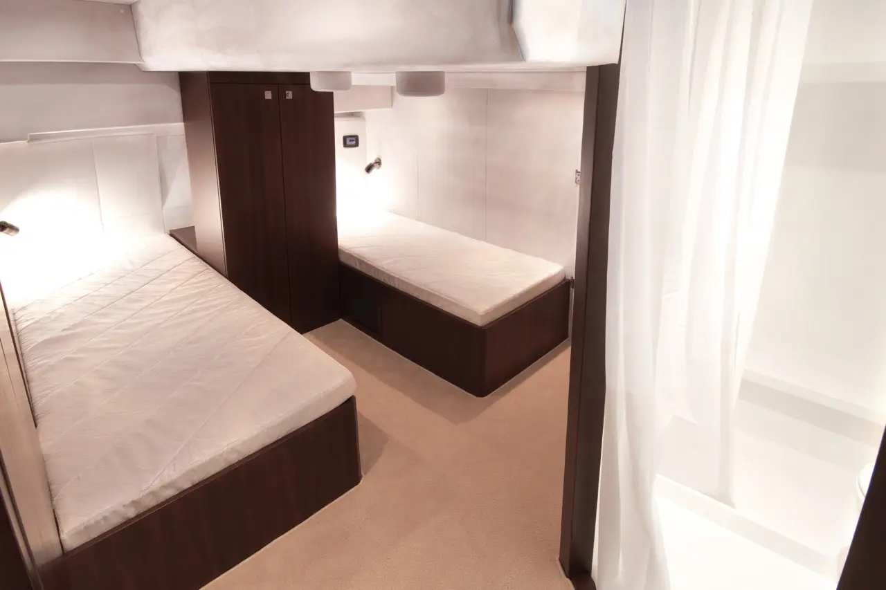 Interior view of a cabin with two twin beds, wooden furniture, and soft lighting, featuring a curtain and closet space.