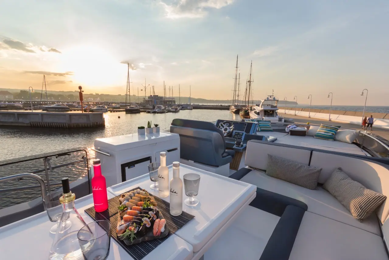Luxury yacht dining setup featuring sushi and drinks at sunset, with a marina and boats in the background.