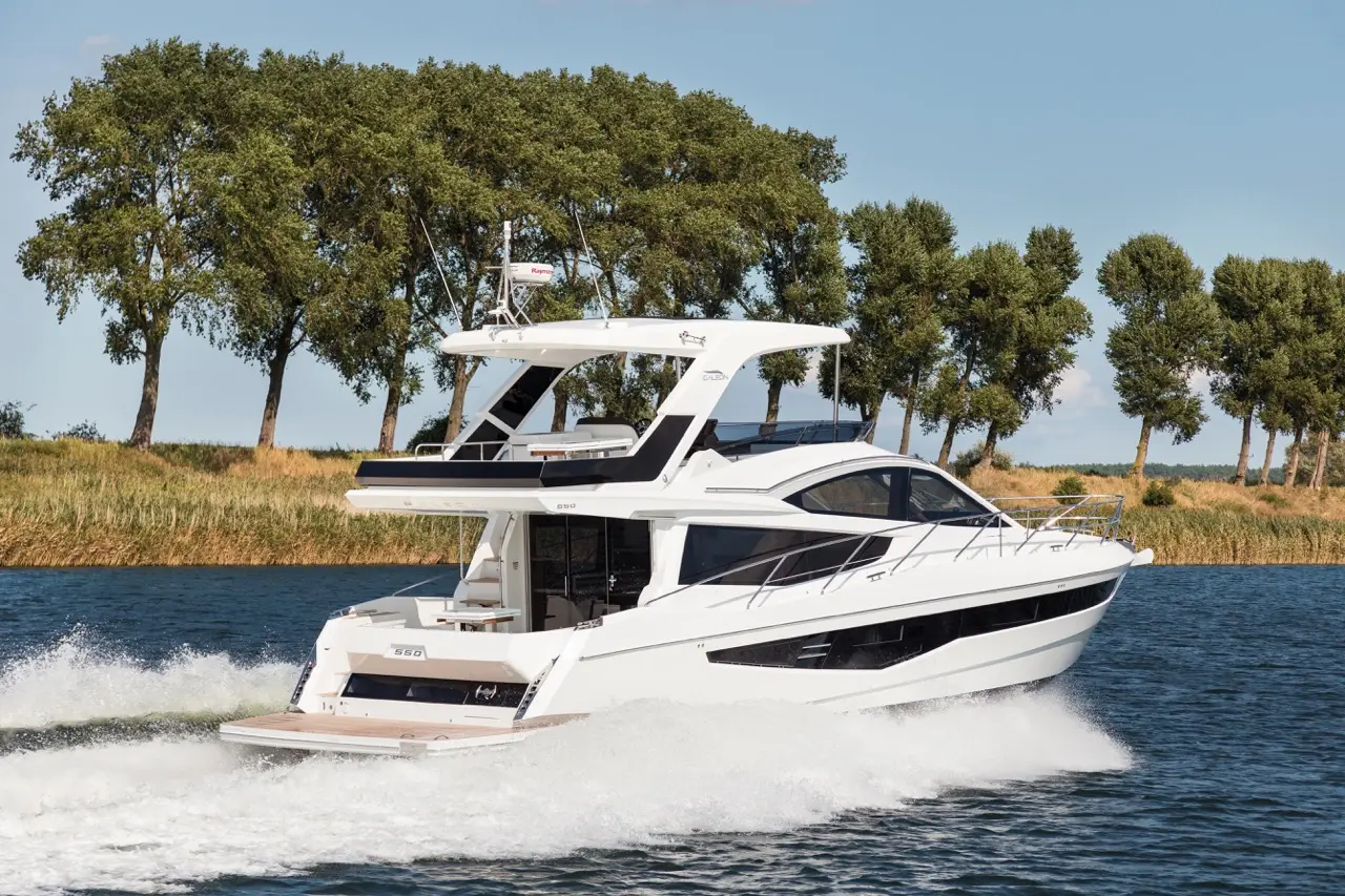 A sleek white luxury boat cruising through blue water, with lush green trees lining the shore and a clear sky above.