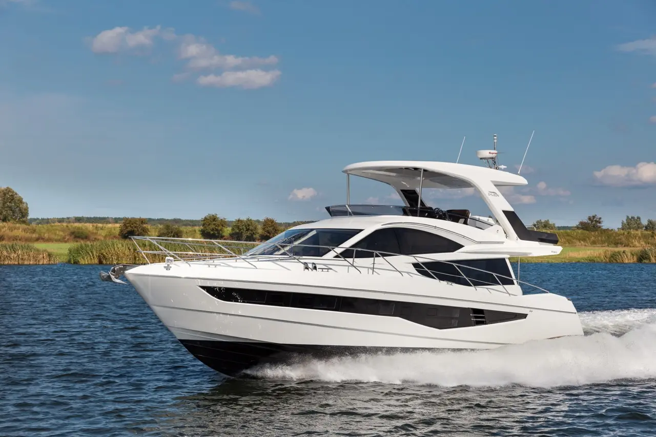 A sleek white yacht cruising on calm water, surrounded by green foliage under a clear blue sky.