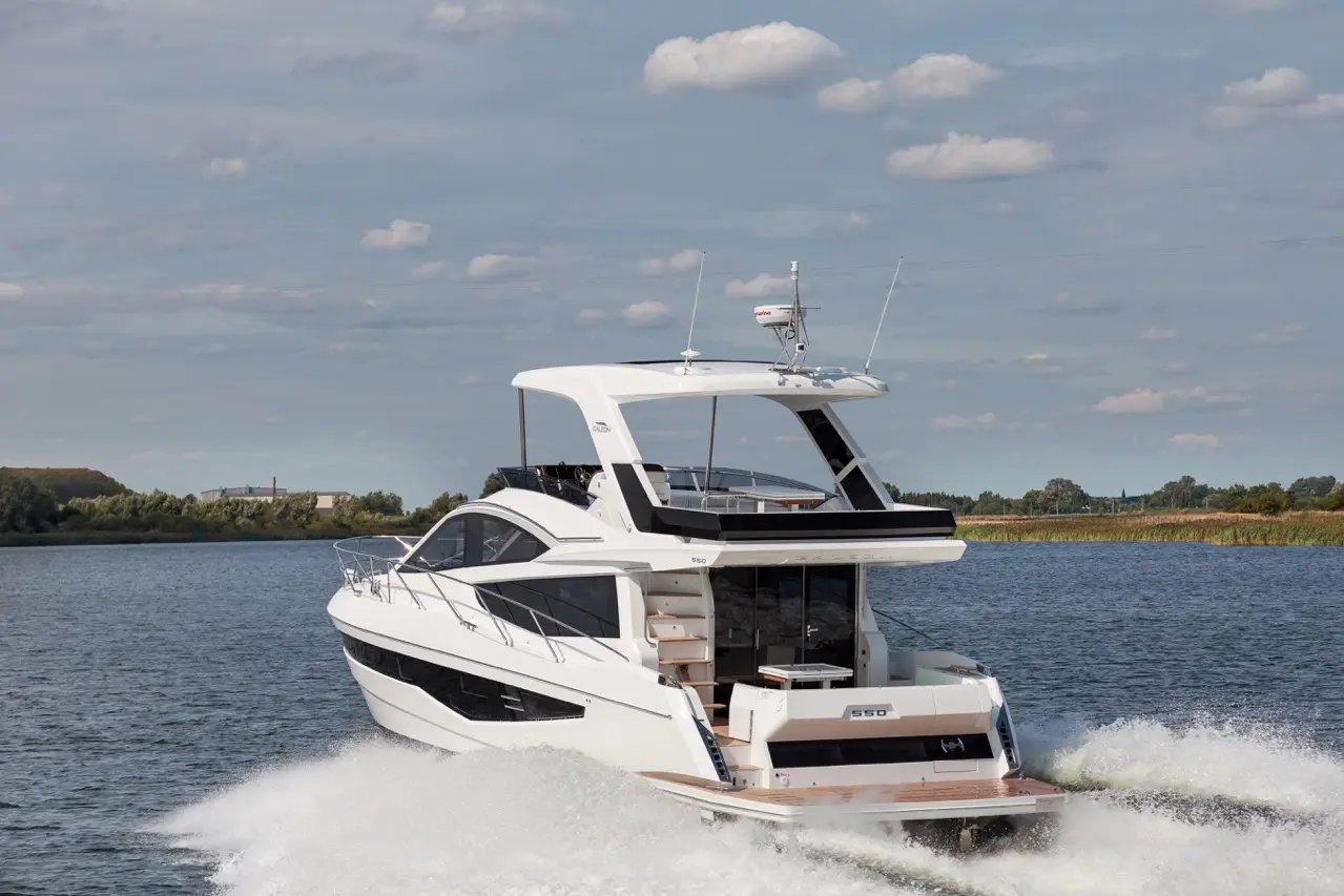 Luxury white yacht cruising on a calm waterway, displaying model number 550 with clear blue skies and light clouds.