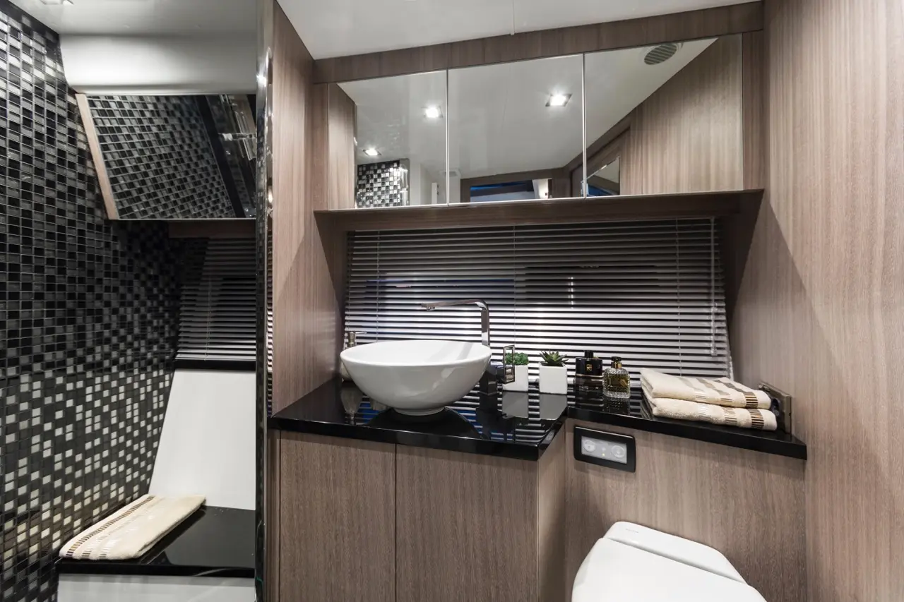 Modern bathroom featuring a black tiled wall, sleek white bowl sink, wooden cabinetry, and decorative plants on the counter.