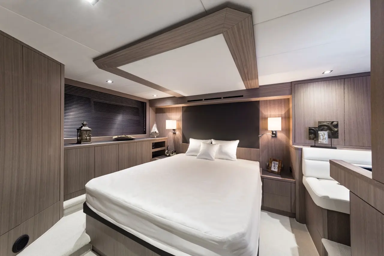 Modern boat cabin featuring a queen-size bed, wooden paneling, ambient lighting, and decorative items on the shelves.