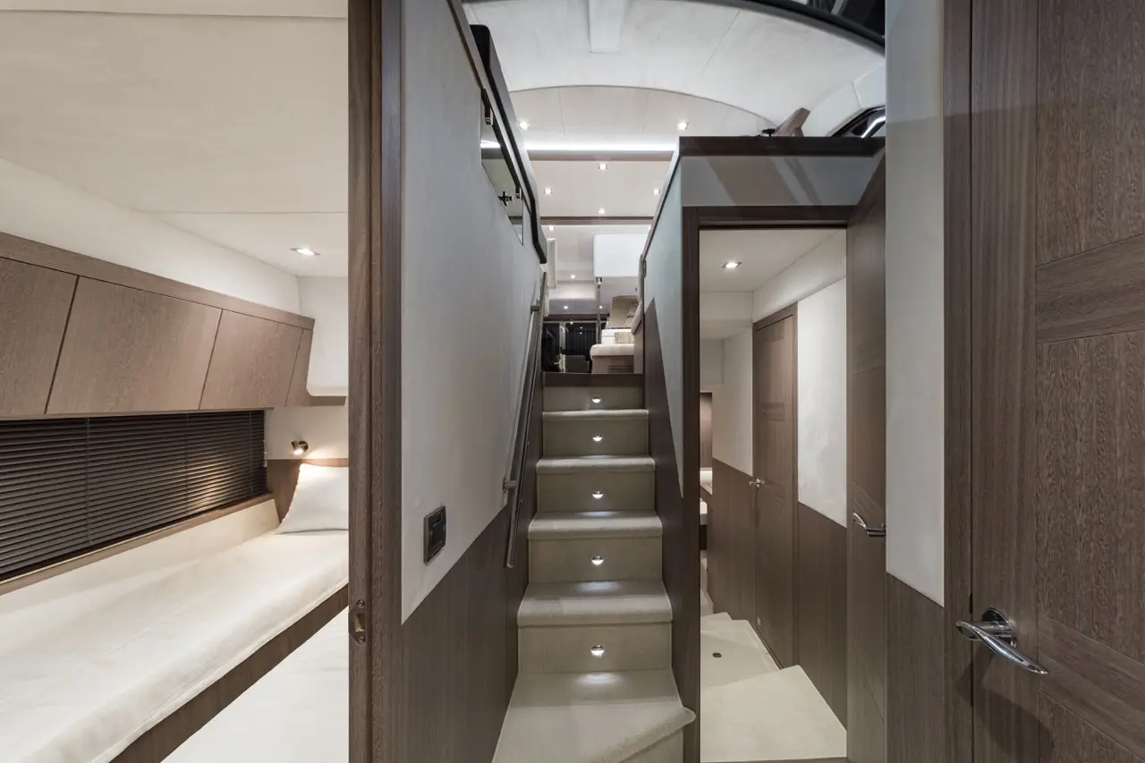 Interior view of a modern yacht featuring a stairway with LED lighting, wooden cabinetry, and a cozy sleeping area.