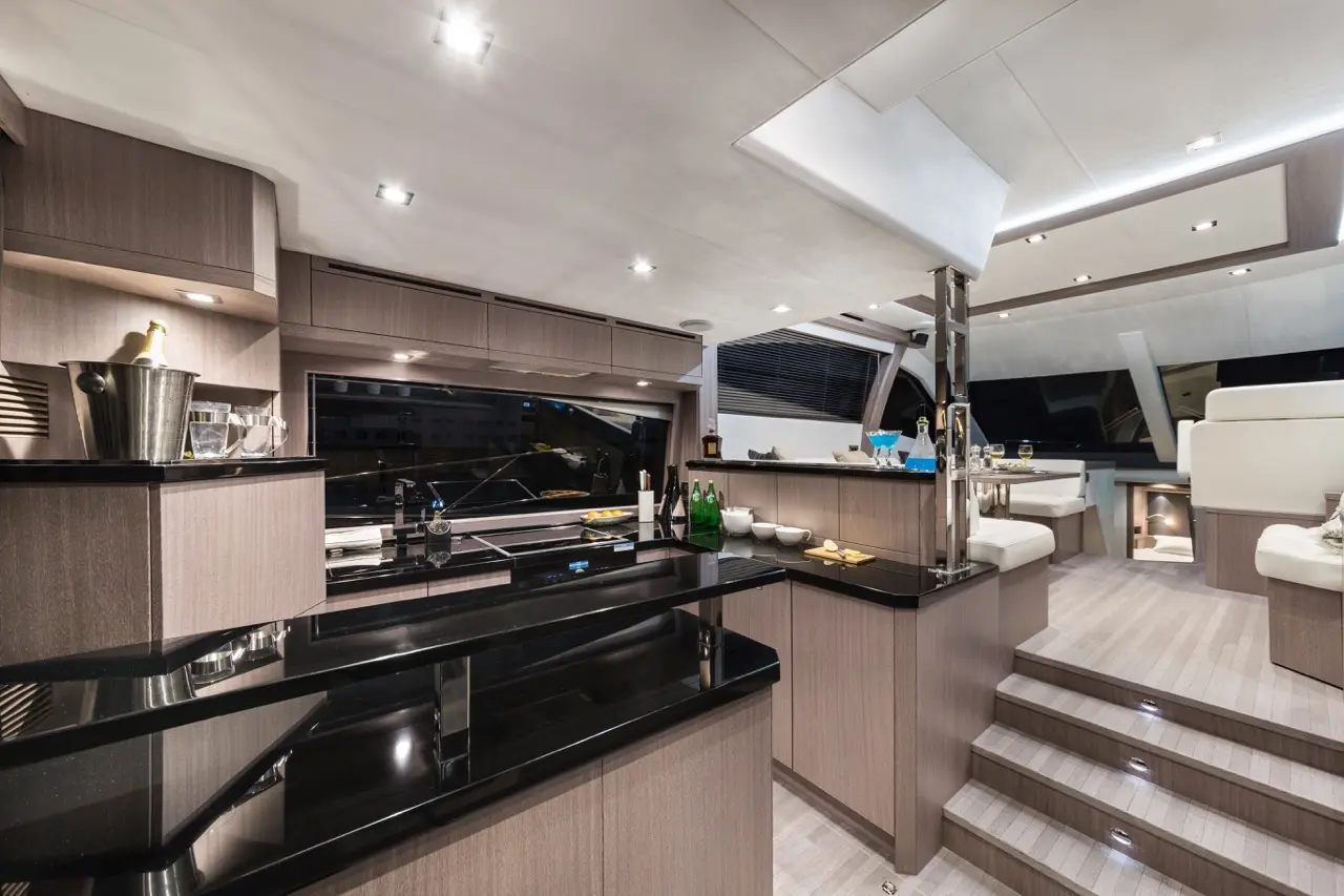 Modern yacht interior featuring a sleek kitchen with black counters, stainless steel accents, and seating area, illuminated softly.