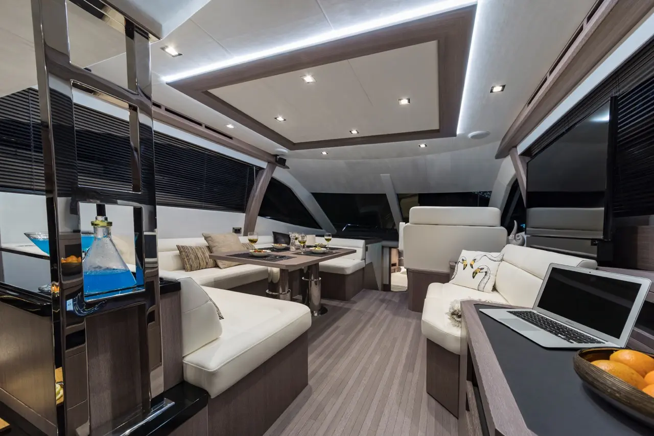 Modern yacht interior with sleek furniture, a dining area, blue drink, laptop, and decorative pillows featuring swans.