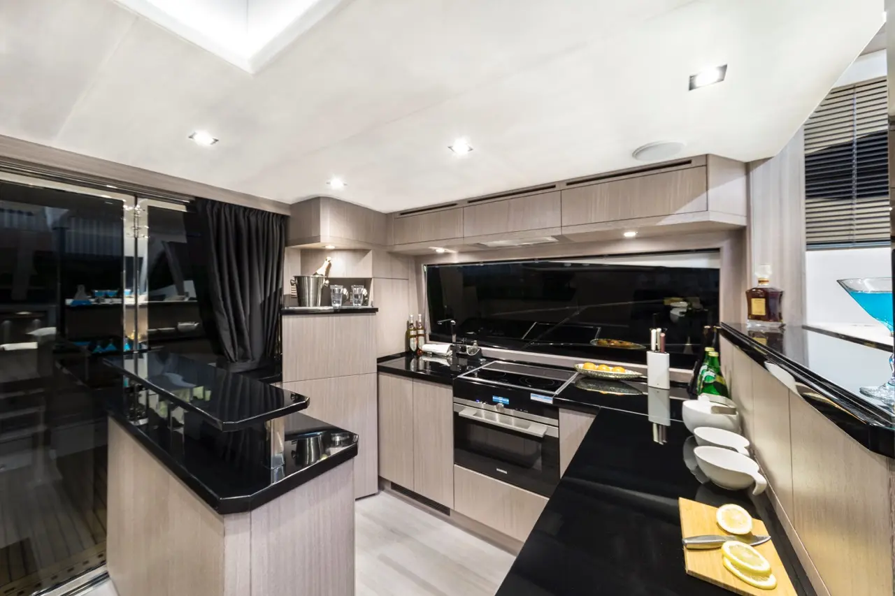 Sleek modern kitchen with black countertops, cooking utensils, and a view of the water through large glass doors.