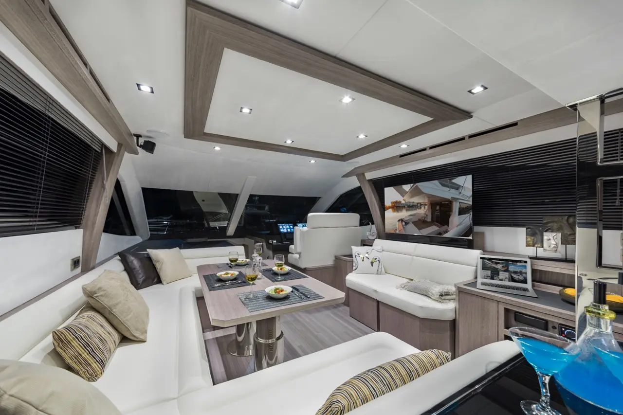 Modern yacht interior with a dining area, white leather seating, decorative pillows, and drinks displayed on the table.